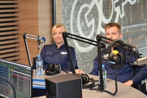 policjantka i policjant siedzą przy stole z zamontowanymi mikrofonami w studiu radiowym