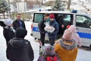 dzieci odbierają prezenty z radiowozu, wewnątrz komendant powiatowy, obok przy radiowozie starosta krakowski