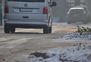 Zbliżenie na zaśnieżoną i oblodzoną nawierzchnię drogi po której porusza się samochód (widać fragment samochodu – widok z tyłu).