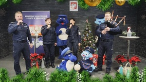 Dwie policjantki i policjant śpiewają. Czwarty policjant gra na dudach.
