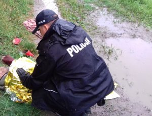 policjant podczas interwencji ratowania wychłodzonego mężczyzny. Policjant schylony okrywa mężczyznę folią srebrno-złotą