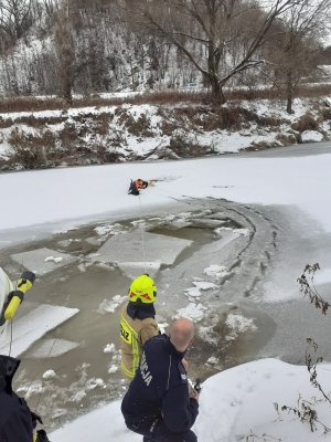 akcja ratunkowa na rzece, policjant na desce ortopedycznej na lodzie trzyma psa i jest ciągnięty za linkę przez druha strażaka  i innego policjanta