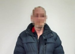 zatrzymany mężczyzna w grantowej kurtce stojący przodem do zdjęcia