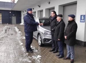 starosta krakowski przekazuje kluczyki od pojazdu komendantowi powiatowemu, obok dwóch samorządowców i nieoznakowany radiowóz