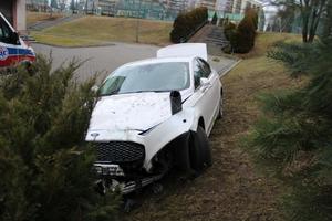 Biały samochód z uszkodzoną pokrywą silnika, stojący częściowo na trawniku, częściowo