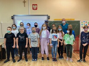 Dzieci oraz nauczyciel w sali lekcyjnej pozują do grupowego zdjęcia z policjantką