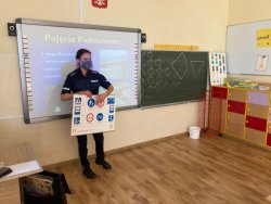 Policjantka w sali lekcyjnej trzyma tablicę edukacyjną ze znakami drogowymi i objaśnia uczniom ich znaczenie