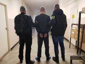 policjanci w ubraniach cywilnych z zatrzymanym w kajdankach