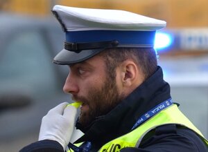 Policjant ruchu drogowego trzyma w ręku gwizdek podejmując ręczną regulację ruchem na drodze