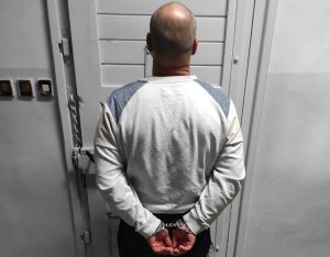 zatrzymany 37-latek stojący tyłem do zdjęcia, ubrany w szarą bluzę z ręakmi w kajdankach trzymanymi z tyłu
