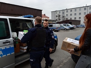 KPP Oświęcim. Policjanci i pracowniczka cywilna przenoszą towary do radiowozu