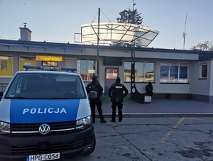 Dwóch umundurowanych policjantów patroluje dworzec autobusowy obok oznakowany radiowóz