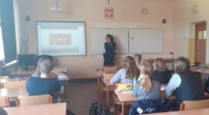 uczniowie siedzący w ławkach podczas prelekcji z policjantką