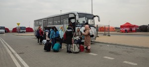 uchodźcy z bagażami wsiadający do policyjnego autokaru