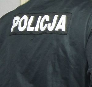 policjant stojący tyłem ubrany w granatową kurtkę z napisem policja