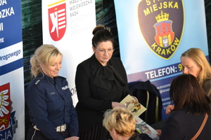 na tle banerów stoi policjantka ruchu drogowego z kobietą wręczając ulotki o bezpieczeństwie