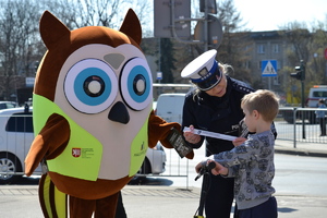 Policjantka ruchu drogowego wraz z maskotką  „Sówką” wręczają chłopcu na hulajnodze element odblaskowy