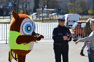 Policjantka ruchu drogowego wraz z maskotką  „Sówką” wręczają kobiecie element odblaskowy oraz ulotkę