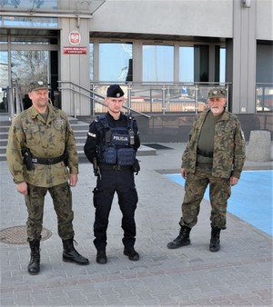 policjant i dwóch strażników PSR przed budynkiem komendy