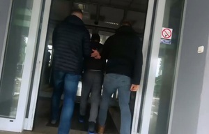 kadr z filmu. Policjanci w ubraniach cywilnych idą z zatrzymanym w kajdankach