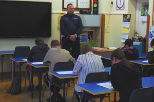 Zdjęcie przedstawia dzieci piszące test, policjant stoi obserwując uczestników konkursu