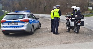 kontrola drogowa - funkcjonariusze drogówki w pobliżu radiowozu, obok motocyklista i pasażer na motocyklu
