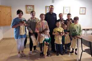 Policjant idzie wzdłuż stołu przy którym siedzą dzieci i rozdaje im maskotki.