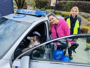 dziewczynka siedząca za kierownica radiowozu pozuje do zdjęcia z z mamą i policjantką