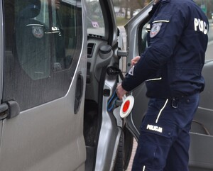 policjant ruchu drogowego trzymając w ręku tarczę do zatrzymywania pojazdów stoi przy busie i przeprowadza kontrolę drogową