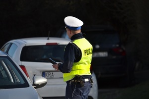 policjant ruchu drogowego stoi na drodze przy samochodach i trzyma w ręku alkomat – urządzenie do badania trzeźwości