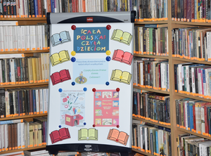 Plakat reklamowy akcji „Cała Polska czyta dzieciom” na tle półek z książkami