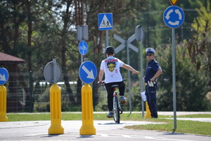 Na miasteczku ruchu drogowego na rowerze jeździ zawodnik, ocenia go policjant ruchu drogowego.