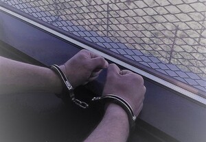 ręce w kajdankach położone na parapecie przy oknie z kratami zdjęcie poglądowe