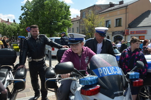 hłopiec na motocyklu policyjnym w białej czapce policjantka ruchu drogowego. W tle dwóch policjantów.
