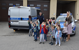 Grupa dzieci wraz z wychowawcą i policjantem stoją na tle dwóch radiowozów