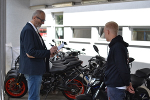 Zawodnik stoi przy motocyklach, mężczyzna go ocenia