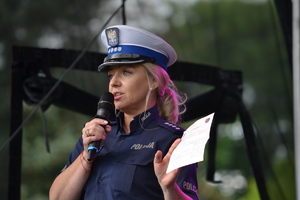 Policjantka ruchu drogowego na scenie trzyma w ręku ulotkę i mikrofon omawiając zasady ruchu drogowego