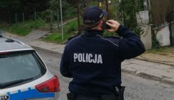 policjant stojący przed radiowozem w czasie sprawdzania osób będących na kwarantannie