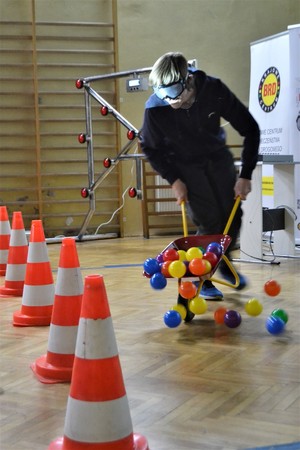 Uczestnik szkolenia biorący udział w części praktycznej – wykonujący zadanie pokonania slalomu w narkogooglach, z taczkami wypełnionymi plastikowymi kulkami.