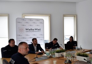 czterech funkcjonariuszy i wójt gminy siedzący przy stole podczas debaty społecznej, za nimi baner gminy Wielka Wieś