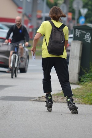 Mężczyzna odjeżdżający na rolkach, trzyma w ręku ulotkę z przepisami. W tle - jadący rowerzysta