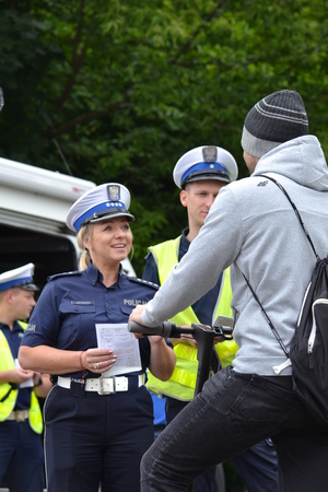 Policjantka ruchu drogowego rozmawia z mężczyzną kierującym hulajnogą elektryczną. W tle - Policjanci ruchu drogowego w żółtych kamizelkach.