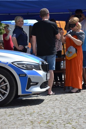 Przedni fragment radiowozu BMW, obok uczestnikcy pikniku sprawdzający działanie alkogogli w towarzystwie policjantki