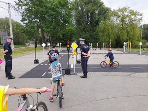 dwóch policjantów ruchu drogowego uczących dzieci na miasteczku rowerowym bezpiecznego poruszania się na drodze