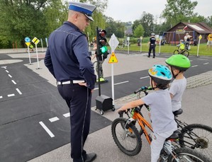 policjant ruchu drogowego uczący dwoje dzieci na miasteczku rowerowym bezpiecznego poruszania się na drodze
