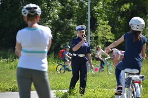 Policjantka ruchu drogowego omawia przez mikrofon błędy popełniane przez rowerzystów i pieszych poruszających się po miasteczku ruchu drogowego.
