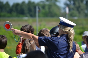 Policjantka ruchu drogowego trzymająca w ręku tarczę do zatrzymywania pojazdów. Wokół dzieci biorące udział w prelekcji.