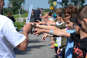 Wójt gminy Kłaj wręcza dzieciom odblaski zapinając je na ręce. Dzieci stoją w rzędzie z wyciągniętymi rękami.