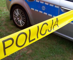 żółta taśma z napisem POLICJA, w tle fragment policyjnego radiowozu