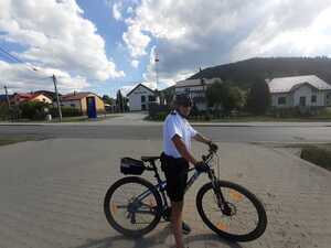 Policjant jedzie na rowerze ścieżką rowerową obok zalewu wodnego